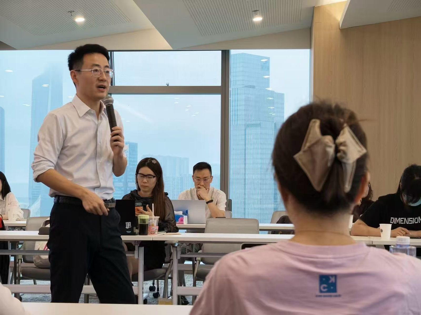 工作坊现场，讲师持话筒面向参会者讲解，参会者在座位上使用电脑记录
